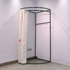 an open shower stall in a corner with white walls and curtains hanging on the wall