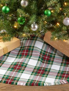 a christmas tree with presents under it on a plaid table cloth and wooden box underneath