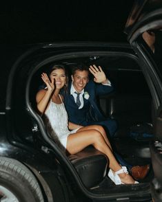 a bride and groom are sitting in the back of a car waving at the camera