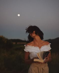 a woman standing in a field holding an open book