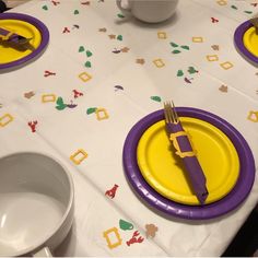 the table is set with purple and yellow plates, silverware, and napkins