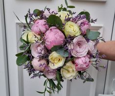 a bouquet of pink and yellow flowers is held up by someone's hand in front of a door