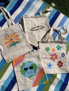 four canvas bags with different designs on them sitting on a striped blanket in the grass