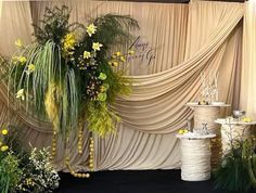 an arrangement of flowers and plants on display in front of a curtained stage backdrop