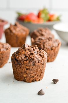 several chocolate muffins sitting on top of a counter next to a bowl of strawberries