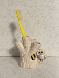 a toothbrush holder with an owl figurine and yellow toothbrush in it