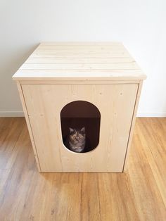 a cat sitting in a wooden house on top of a hard wood floor next to a white wall