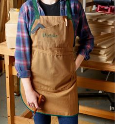 a woman wearing an apron and holding a wood mallet in her hands while standing next to a workbench