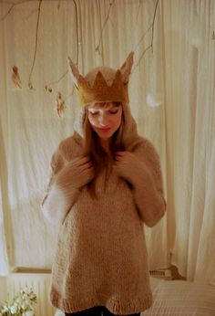 a woman wearing a knitted sweater with a crown on her head standing in front of a curtain