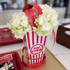 a popcorn bucket filled with white flowers on top of a counter next to a red tray