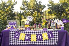 a table with purple and yellow decorations for a game day party in the park on a sunny day