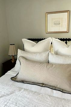 a bed with white pillows and black headboard next to a painting on the wall