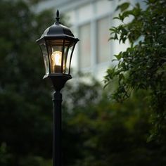 an old fashioned lamp post with a light on it's side and trees in the background