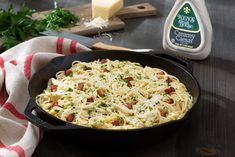 a skillet filled with pasta and parmesan cheese on top of a wooden table