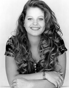 a black and white photo of a woman with long curly hair smiling at the camera