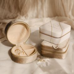 two wedding rings are in a box on a white tableclothed cloth with gold trimmings