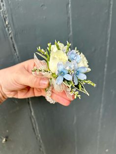 a person's hand holding a bouquet of blue and white flowers in front of a gray door