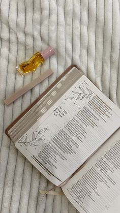 an open book sitting on top of a bed next to a small bottle of oil