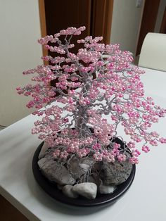 a bonsai tree with pink flowers and rocks on a white tablecloth covered table