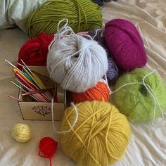 several balls of yarn sitting on top of a bed next to crochet hooks