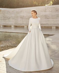 a woman in a white wedding dress standing by a fountain with her hands on her hips