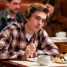 a young man sitting at a table in front of a plate of food and coffee