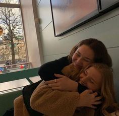 two women hugging each other in front of a window