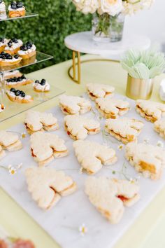 a table topped with cookies and pastries on top of a white tray next to flowers