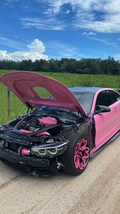 a pink car with its hood open on the side of a road next to a grassy field