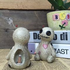 two ceramic figurines sitting next to each other in front of books and a potted plant