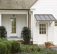 a white house with two doors and some plants on the front porch, along with potted shrubs