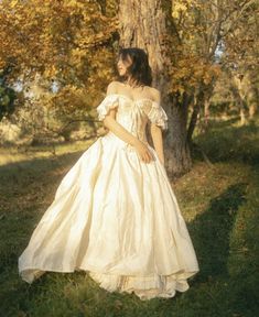 a woman in a white dress standing next to a tree