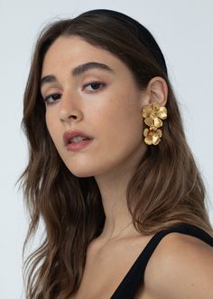 a woman with long brown hair wearing gold earrings and black dress looking off to the side