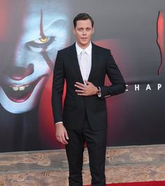 a man in a suit standing on a red carpet with his hands on his chest