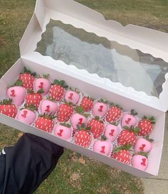 a person holding a box full of strawberries with pink frosting and hearts on them