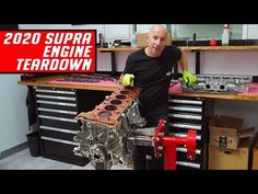 a man standing next to an engine in a room with tools on the table and shelves behind him