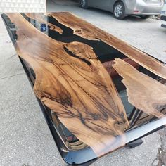 a wooden table sitting on top of a parking lot next to a silver car parked in front of it