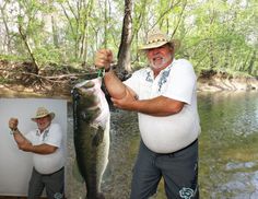 an older man holding a large fish while standing next to a river