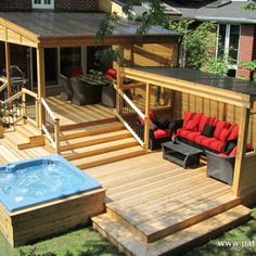 a hot tub sitting on top of a wooden deck next to a patio and covered in red cushions