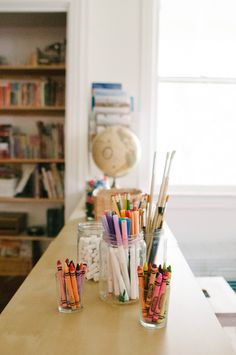 there are many different colored pencils in glass jars on the counter next to bookshelves