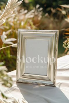 a silver frame sitting on top of a white cloth covered table next to tall grass