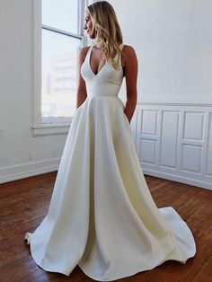 a woman standing in front of a window wearing a white dress with pockets on the side