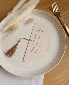 a white plate topped with a menu next to a gold fork and knife on top of a wooden table