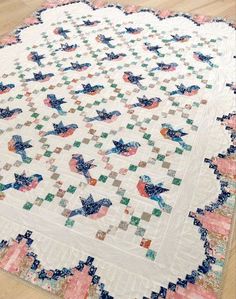 a white quilt with blue, pink and green designs on the center is laying on a wooden floor