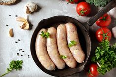 four sausages in a frying pan surrounded by vegetables and garlic on a table