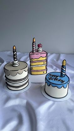 three birthday cakes sitting on top of a white sheet