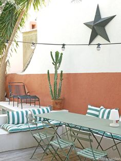 an outdoor dining area with green and white striped chairs, table and potted cactus