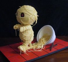 a sculpture made out of noodles sitting on top of a red mat next to a white bowl