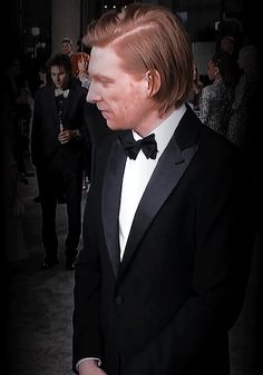 a man in a tuxedo and bow tie standing next to other people at an event