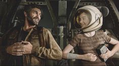 two people standing next to each other in front of a space station with one person wearing an astronaut's helmet